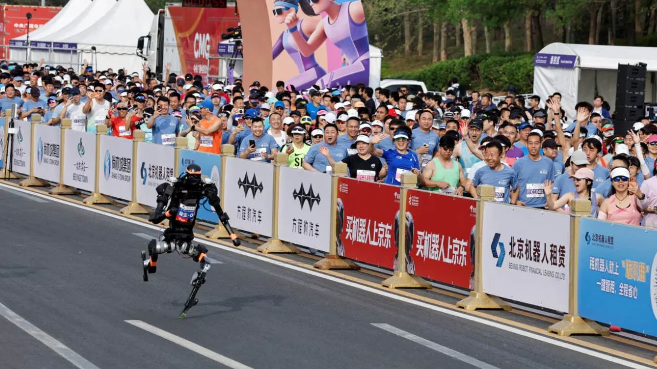 Robot humanoïde bipède courant sur la piste du semi-marathon de Yizhuang à Pékin, devant une foule de spectateurs et de coureurs humains derrière les barrières publicitaires.